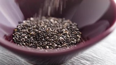 Kurutulmuş chia tohumları yavaş çekimde kırmızı bir seramik kaseye düşüyor. Omega 3 besinli diyet süper yiyecekler.