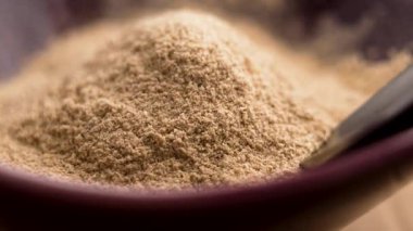 Bambu kaşığı kırmızı bir seramik kaseden Ashwagandha kökü tozu topluyor. Ayurvedic anti-stres ilacı