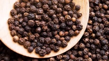 Ahşap kaşıkta baharatlı baharatlı biber. Aromatik desenli kırışık taneler. Döndürme