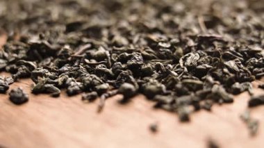 Tahta masanın üzerine kurumuş yeşil çay yaprakları dökülüyor.