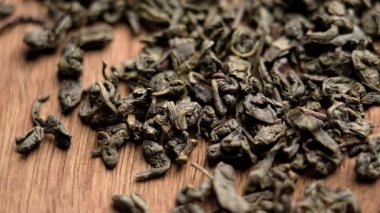 Ahşap dokuya geleneksel Çin yeşil çayının kurutulmuş kıvrımlı yaprakları. Makro atış. Döndürme