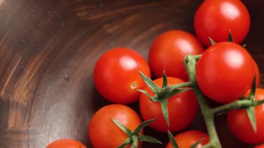Yeşil yapraklı taze kırmızı domatesler yavaş çekimde ahşap bir kaseye düşüyor.