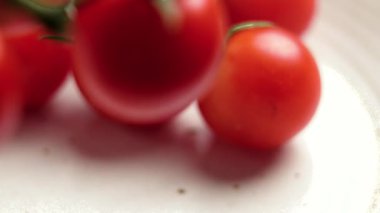 Taze kırmızı kiraz domateslerini yeşil yapraklı mutfak tabağına koymak. Sebzeli organik malzeme.