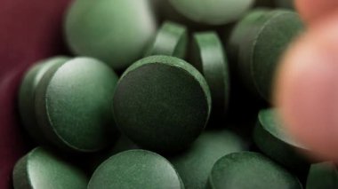 Kırmızı seramik kasede yeşil spirulina yosun tabletleri ve bir hap yutan parmaklar. Organik iyileştirme malzemeleri. Makro
