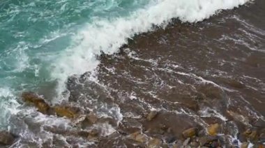 Köpüklü mavi dalgalar kumlu sahile yavaş çekimde kayalarla vuruyor.