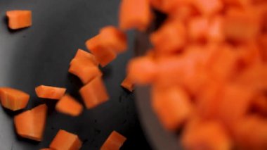 Siyah seramik bir tabağa düşen taze, doğranmış havuçların yavaş hareketi. Doğranmış organik sebzeler