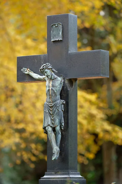 cross with jesus figure without left arm and with broken neck in autumn cemetery