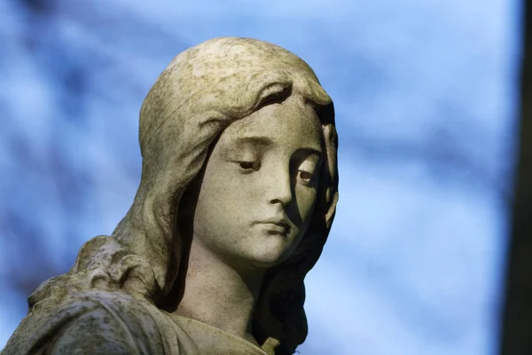 beautiful statue of a young woman with sad look to the ground on a cemetery