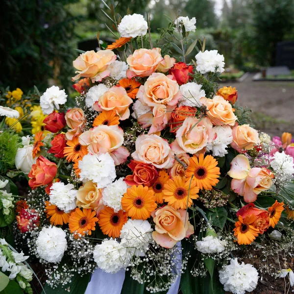stylish funeral flowers of white carnations, orange gerbera and red and pink roses on a grave after a funeral
