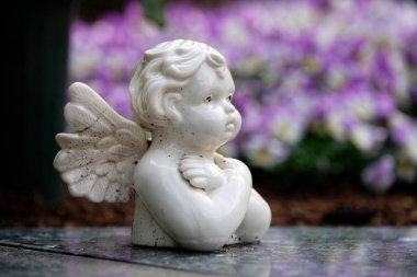 Renkli bahar çiçeklerinin önündeki bir mezar taşının üzerinde bulanık arkaplanda küçük kirli beyaz bir putto.