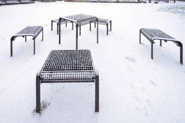 Parkta hafif bir kar yağışı sonrası modern metal banklar.
