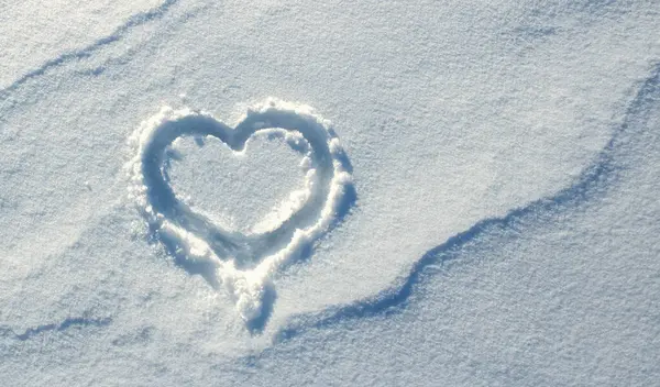 Top view, hand-drawn a heart on natural pure white soft snow surface. Symbol of love in winter holiday season.