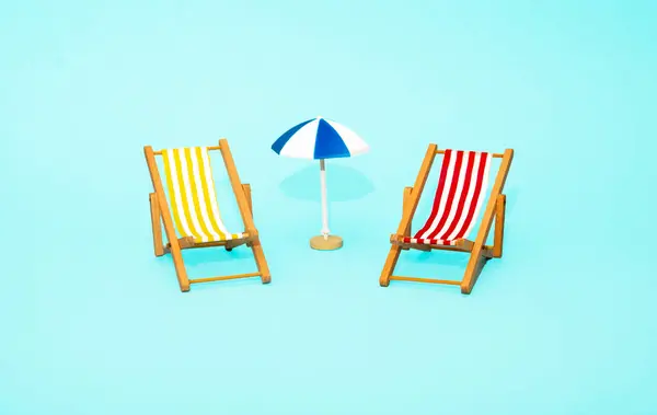 Plaj rahatlaması ve tatil konsepti. Oyuncak güneş şezlongu ve şemsiye mavi renkli kağıt arka planda.