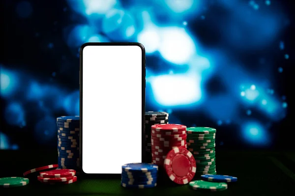 Casino. Online casino. Game chips and dice lie on a table next to a smartphone against a blurred dramatic background. Online poker. Free space. Game chips for betting in gambling. Dice. Poker chips.
