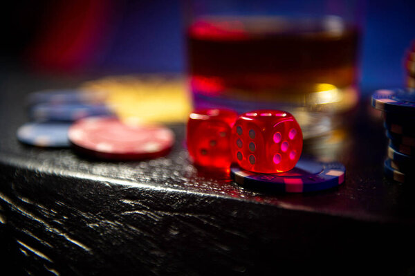 The dice sit on the gambling betting chips on a black wooden surface. Blurred background. Dice on blurred bokeh background.