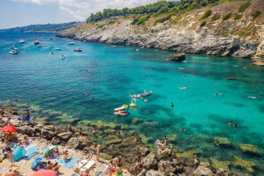 15 Ağustos 2023 - Santa Cesarea Terme, Salento, Puglia, İtalya. Porto Miggiano 'nun inanılmaz körfezi. Turist ve teknelerle dolu, berrak, mavi ve turkuaz denizde. Yüksek kayalıkların arasında küçük bir sahil var.