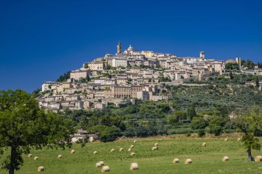 İtalya 'nın Umbria eyaletindeki Trevi köyünün panoramik manzarası. Şehrin antik taş evleri, tepenin üzerine tünemişti. Taze biçilmiş saman balyalarıyla dolu bir tarla..