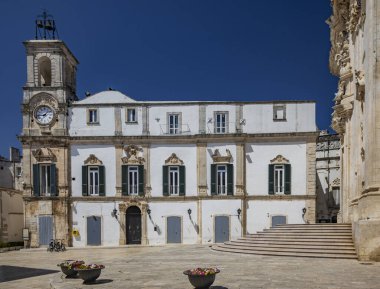 Martina Franca, Taranto, Puglia, İtalya. Barok mimarisi olan bir köy. Üniversite Sarayı, çan kulesi olan, güzel Piazza Plebiscito 'da. Yazın güneşli bir günde mavi gökyüzü.