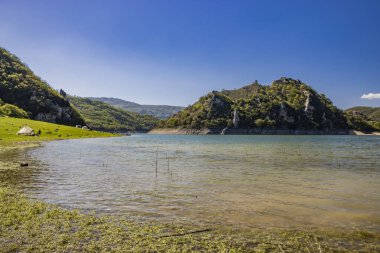 Turano Gölü manzaralı, İtalya 'nın Castel di Tora, Rieti, Lazio köyünde. Bazı insanlar yeşil dağlarla çevrili gölde kamp yapmaya gider. Yazın mavi gökyüzü.