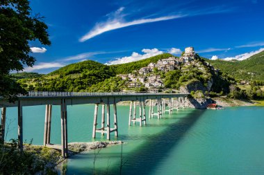 Turano Gölü manzaralı, İtalya 'nın Castel di Tora, Rieti, Lazio köyünde. Gölün merkezini çevreleyen uzun köprü yeşil dağlarla çevrilidir. Yazın mavi gökyüzü.