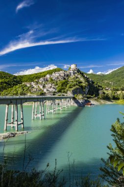 Turano Gölü manzaralı, İtalya 'nın Castel di Tora, Rieti, Lazio köyünde. Gölün merkezini çevreleyen uzun köprü yeşil dağlarla çevrilidir. Yazın mavi gökyüzü.