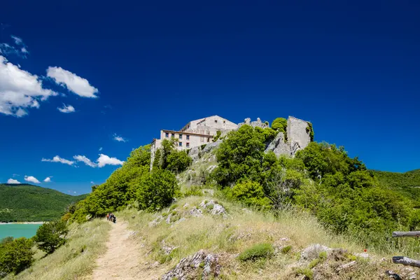 Antuni Dağı 'ndaki kale, Turano Gölü' ndeki Castel di Tora, Rieti, Lazio, İtalya yakınlarındaki köy. Issız köy, yeşil dağlarla çevrili gölün merkezinde duruyor..