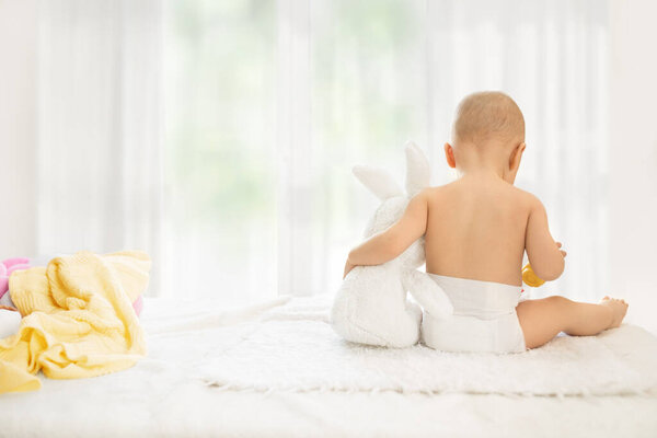 Младенец в пеленках обнимает мягкого кролика, спина виляет