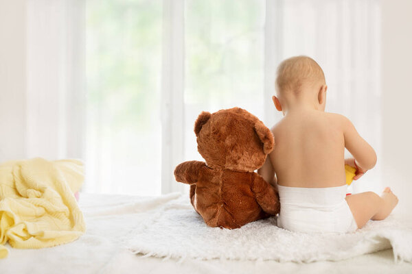 Little baby with her adorable soft toy on bed. Babyhood. Back view