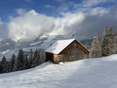Indigenous alpine huts and wooden cattle stables in the Swiss Alps covered with fresh first snow over the Lake Walen or Lake Walenstadt (Walensee), Amden - Canton of St. Gallen, Switzerland / Schweiz