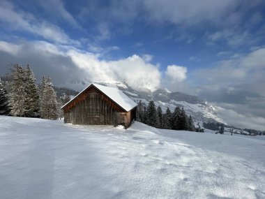 Indigenous alpine huts and wooden cattle stables in the Swiss Alps covered with fresh first snow over the Lake Walen or Lake Walenstadt (Walensee), Amden - Canton of St. Gallen, Switzerland / Schweiz
