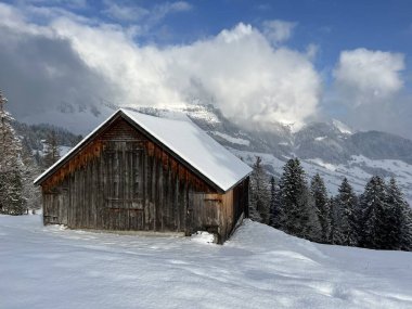Indigenous alpine huts and wooden cattle stables in the Swiss Alps covered with fresh first snow over the Lake Walen or Lake Walenstadt (Walensee), Amden - Canton of St. Gallen, Switzerland / Schweiz