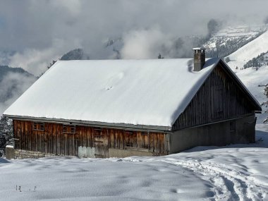Indigenous alpine huts and wooden cattle stables in the Swiss Alps covered with fresh first snow over the Lake Walen or Lake Walenstadt (Walensee), Amden - Canton of St. Gallen, Switzerland / Schweiz