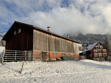 Old traditional swiss rural architecture and alpine livestock farms in the winter ambience over the Lake Walen or Lake Walenstadt (Walensee) and in the Swiss Alps, Amden - Canton of St. Gallen, Switzerland / Schweiz