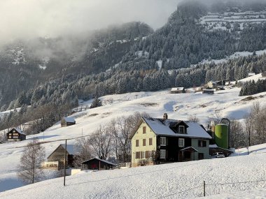 Old traditional swiss rural architecture and alpine livestock farms in the winter ambience over the Lake Walen or Lake Walenstadt (Walensee) and in the Swiss Alps, Amden - Canton of St. Gallen, Switzerland / Schweiz