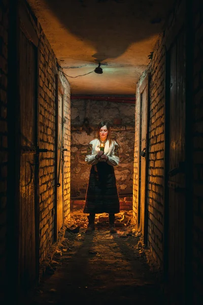 一个身着乌克兰传统服装的女孩站在黑暗的地下室里 手里拿着蜡烛 乌克兰的悲剧 炮轰战 垂直照片 图库图片