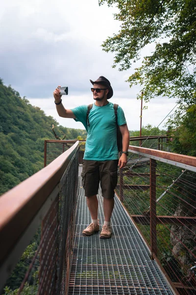 在佐治亚州Okatse峡谷的男性游客 沿着悬挂在陡峭悬崖之上的金属人行道行走 夏日时分 在智能手机上自私自利垂直照片 — 图库照片