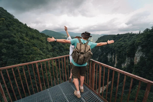 Kadın ve erkek. Mutlu çift, Okatse Kanyonu, Georgia 'da gezginler, derin uçurumun yukarısında asılı metal yaya yolu üzerinde duruyorlar. Deri şapka. Seyahat ve tatil. Arka plan.