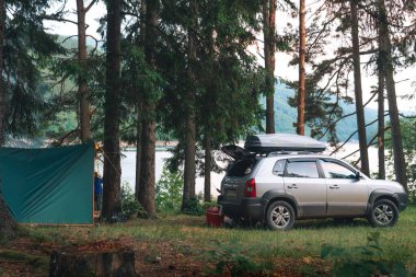 Kamp, vahşi doğada kamp. Arabayla seyahat ve turizm. Uzun kozalaklı ağaçların yanında bir araç. Karpat Dağları 'nda çadırlar ve aktif eğlence.