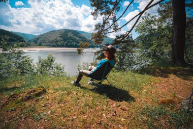 Kız göle bakan dağdaki manzaranın tadını çıkarıyor. Portatif kamp sandalyelerinde oturuyorlar. Turizm ve tatil için ekipman kavramı. Etkin yaşam biçimi