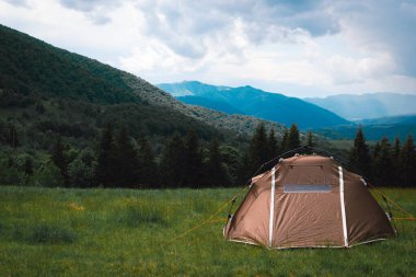 Hızlı bir sistemi olan kahverengi bir turist çadırı bir dağın tepesinde duruyor. Harika sıcak bir yaz sabahı, özgürlük ve seyahat kavramı..