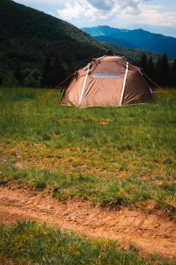 Hızlı bir sistemi olan kahverengi bir turist çadırı bir dağın tepesinde duruyor. Harika, sıcak bir yaz sabahı, özgürlük ve seyahat kavramı. Karpatlar, Prislop Geçidi, Ukrayna. Dikey fotoğraf