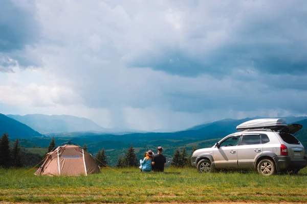 在山顶上 一对夫妇 一男一女 正在欣赏群山的美景 一个旅游帐篷和一辆四轮驱动汽车 车顶有车架 自由和旅行的概念 乌克兰 图库图片
