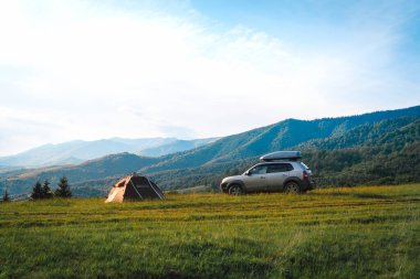 Dağın tepesinde bir turist çadırı ve çatısı olan dört tekerli bir SUV aracı var. Özgürlük ve araba ile seyahat kavramı, Ukrayna
