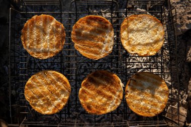 Round buns, lying in rows on the metal grid of the wood-fired grill. The concept of cooking, frying hamburgers. Coal and heat. Top down view.