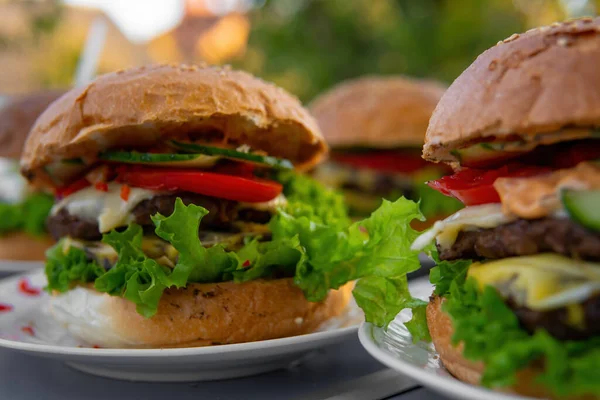 Big, nice hamburgers with a double patty, fresh vegetables and grilled meat. Sunny day outdoors. Concept of tasty street food. Selective focus