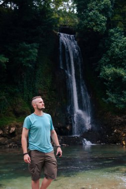 A man, a tourist, a traveler enjoys the wonderful nature. Stones in a mountain river. Vertical photo. Vacation and tourism. Abhesi waterfall.