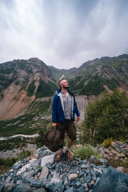 Elinde askeri sırt çantasıyla bir yürüyüşçü dağın tepesinde tek başına duruyor. Kafkas dağları, Svaneti, Georgia. Yaz. Chalaadi buzuluna giden yol. Dikey fotoğraf.