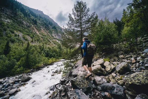 一个背着背包的远足者 一个旅行者 独自行走 从巨石走到石头 高加索山脉 湍急的河流 Svaneti Georgia 夏季云雨季节 图库图片