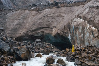 Bulutlu ve yağmurlu havada tek başına bir turist yürüyüş yolunun bitiş noktasına ulaştı. Sarı yağmurluk. Svaneti bölgesinde bulunan Chalaadi buzulu, Gürcistan, Kafkasya.