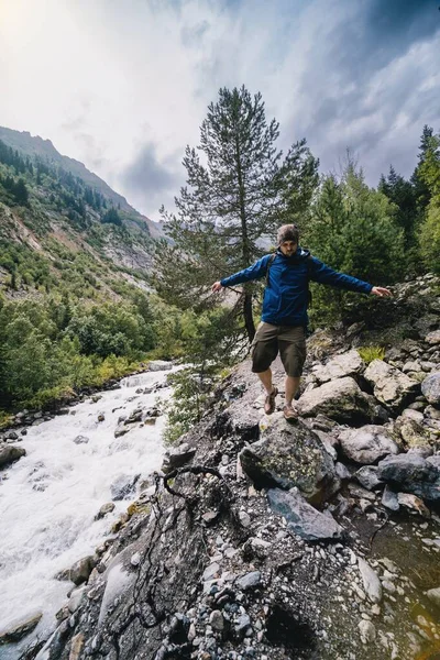 一个背着背包的远足者 一个旅行者 独自行走 平衡着从巨石到石头的脚步 高加索山脉 湍急的河流 Svaneti Georgia 夏天的云雨季节 垂直照片 — 图库照片